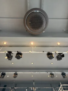 Circular ceiling ventilation unit installed above stage lighting in a commercial space