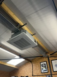 Suspended ceiling cassette air conditioning unit installed in a workshop with exposed beams.