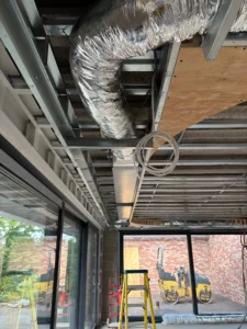 Air conditioning ductwork installed along an exposed ceiling frame above sliding doors.