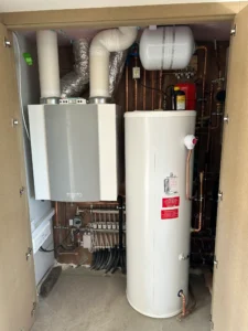 Heat pump hot water cylinder and plant room components installed inside a utility cupboard.