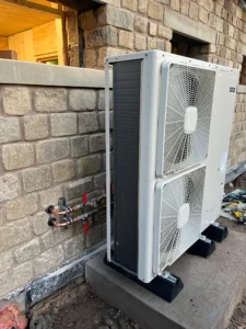Air source heat pump installed externally on a concrete base beside a stone wall.