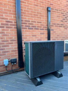 Samsung air source heat pump installed on raised brackets beside a red brick exterior wall